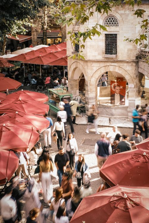 Free Crowded market scene with people walking under red umbrellas in an outdoor setting. Stock Photo