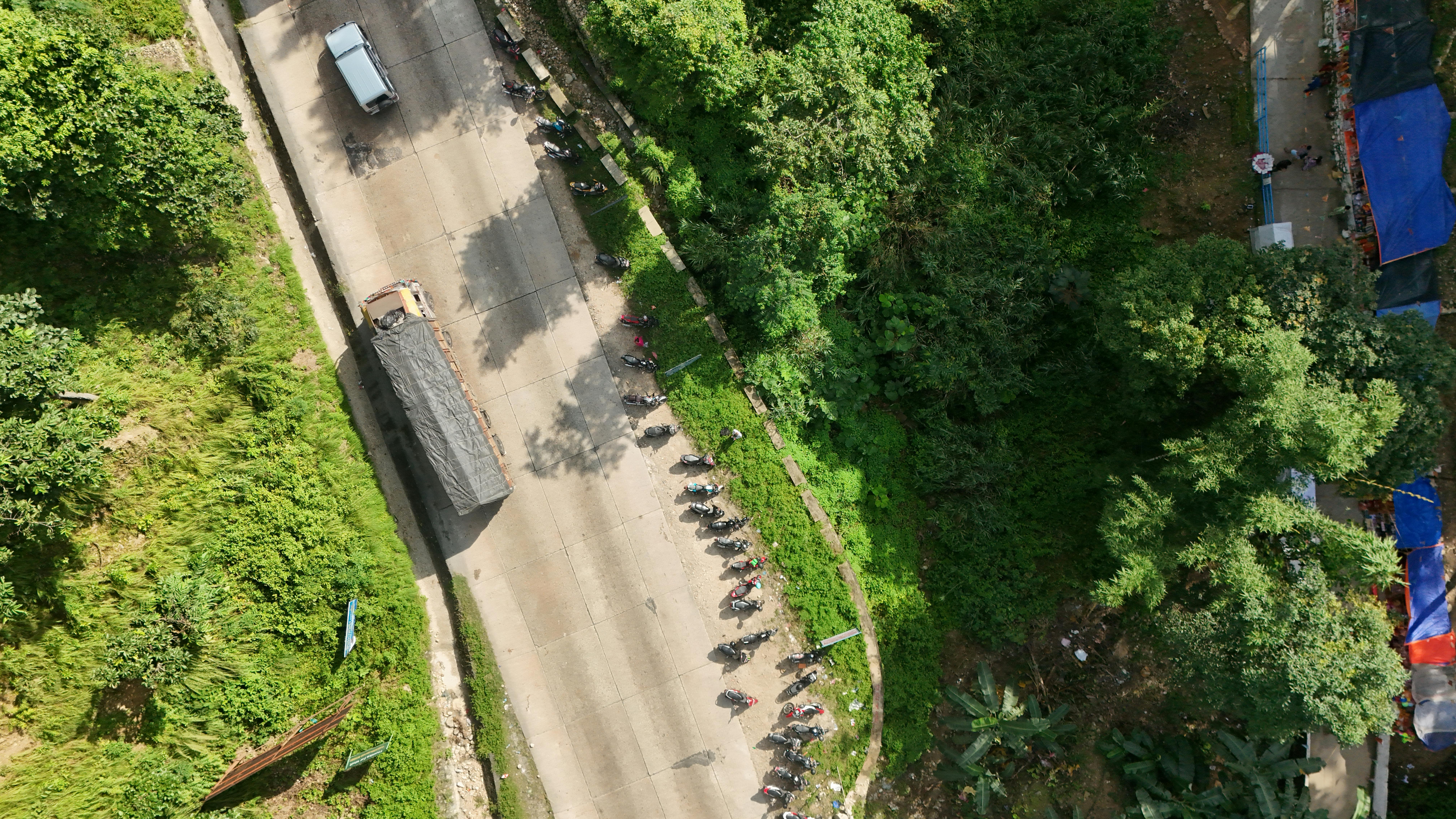무료 무성한 녹지로 둘러싸인 주차된 차량이 있는 도로의 공중 촬영으로, 고요한 풍경이 연출됩니다. 스톡 사진