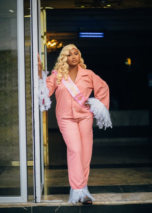 Free Fashionable woman in pink pajamas with feather details standing confidently in a doorway. Stock Photo