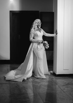 Stylish black and white photo of a bride in an elegant lace gown indoors.