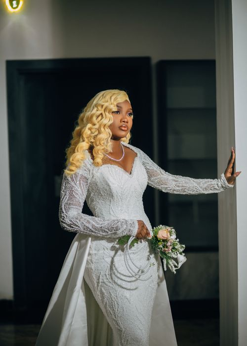Free A beautiful bride in a lace wedding gown holding a bouquet indoors. Stock Photo