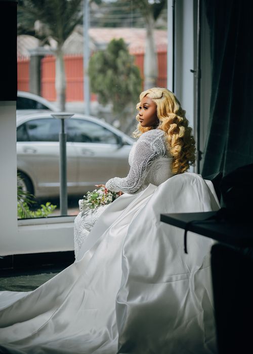 Free Stunning bride in a luxurious white gown posing gracefully by a window, embracing elegance. Stock Photo