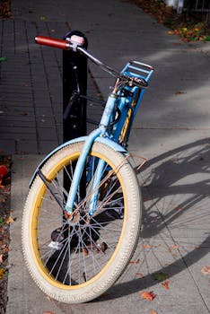 A vintage bicycle with worn-out tires locked to a pole on a city street in daylight.