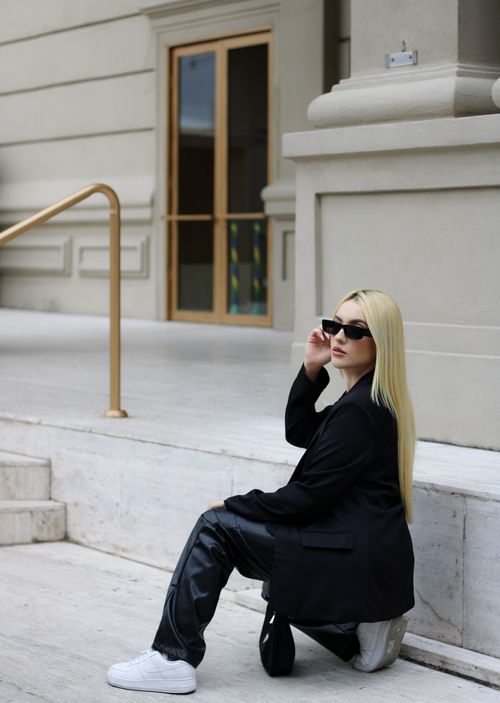 Free Chic woman in sunglasses and black jacket poses confidently on city steps. Stock Photo