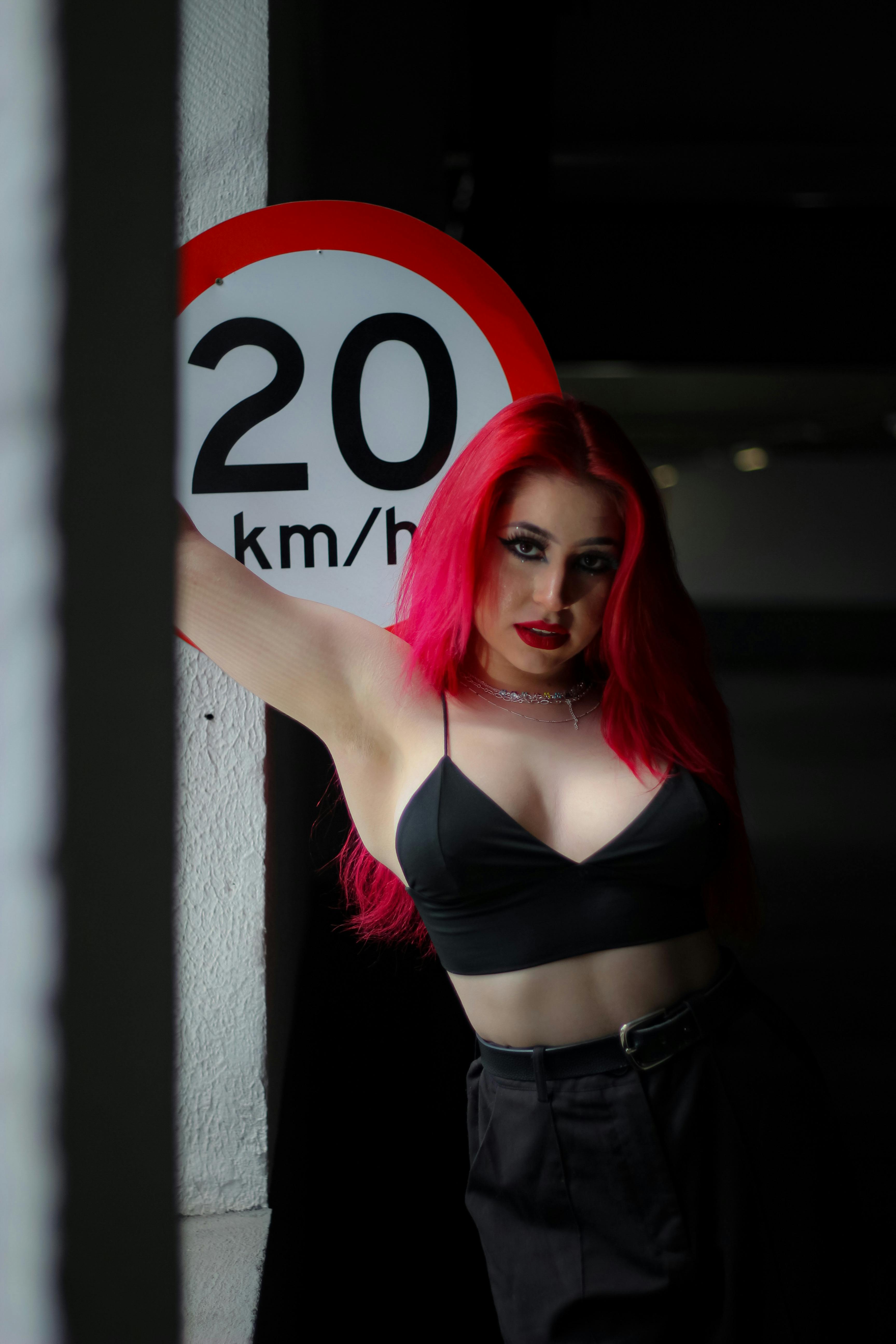 Striking fashion portrait of a woman with vibrant red hair posing by a speed limit sign.