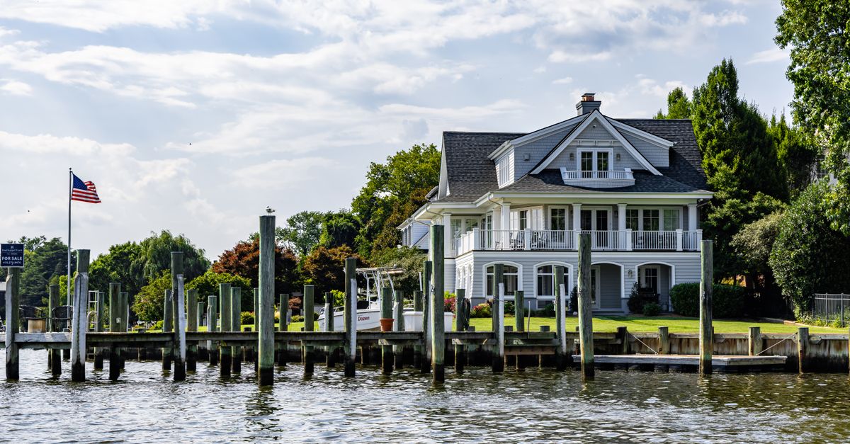 A lovely waterfront home with a dock and American flag on a sunny summer day.