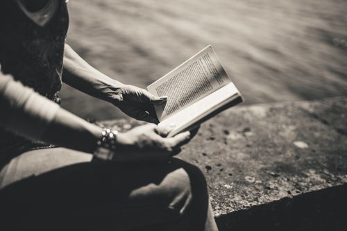 Free A woman enjoys reading a book outdoors by the water in a monochrome setting. Stock Photo