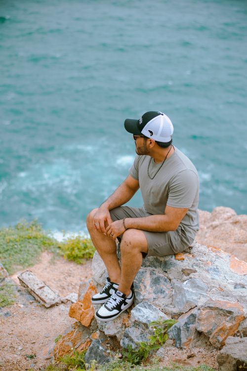 Free A man sits on a rocky cliff overlooking the ocean, enjoying a serene moment. Stock Photo