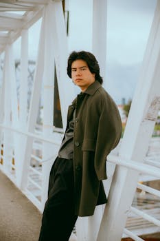 Fashionable young man in coat standing on a city bridge, exuding a confident and casual style.