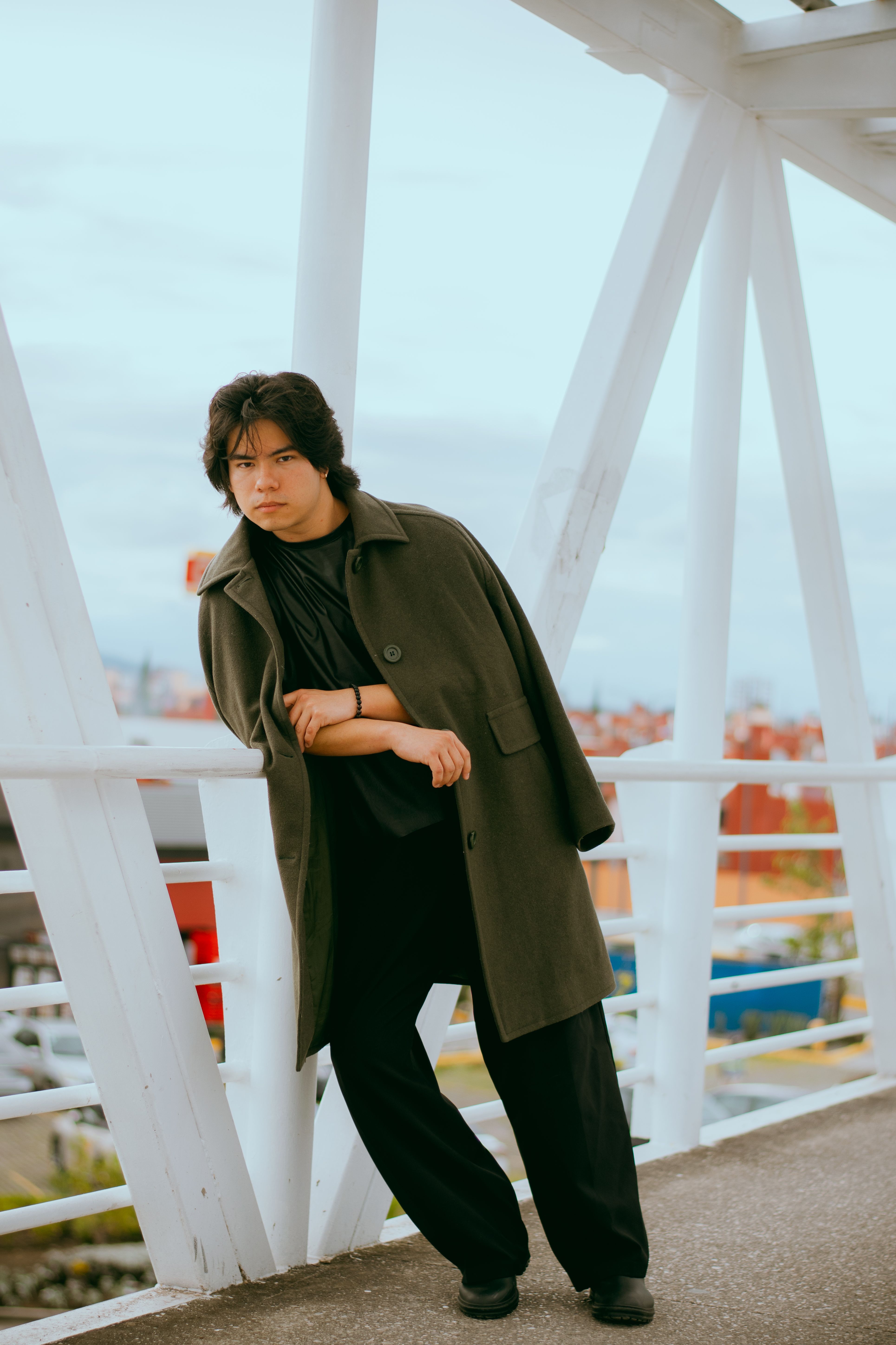 Young adult posing stylishly on a modern bridge outdoors in casual attire.