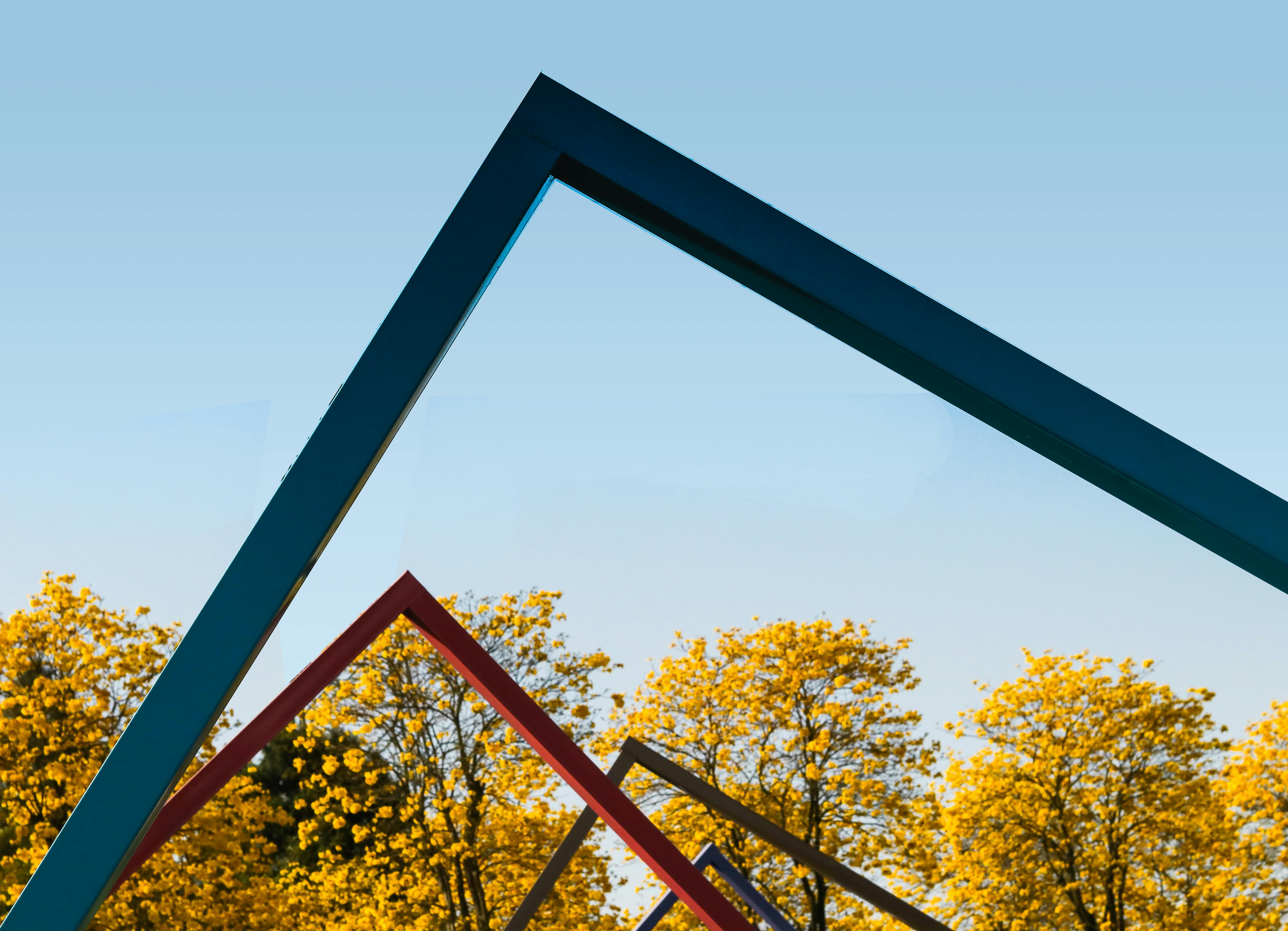 Bezpłatne Żywe geometryczne kształty oprawiają czyste, błękitne niebo nad złotymi jesiennymi drzewami. Zdjęcie z galerii