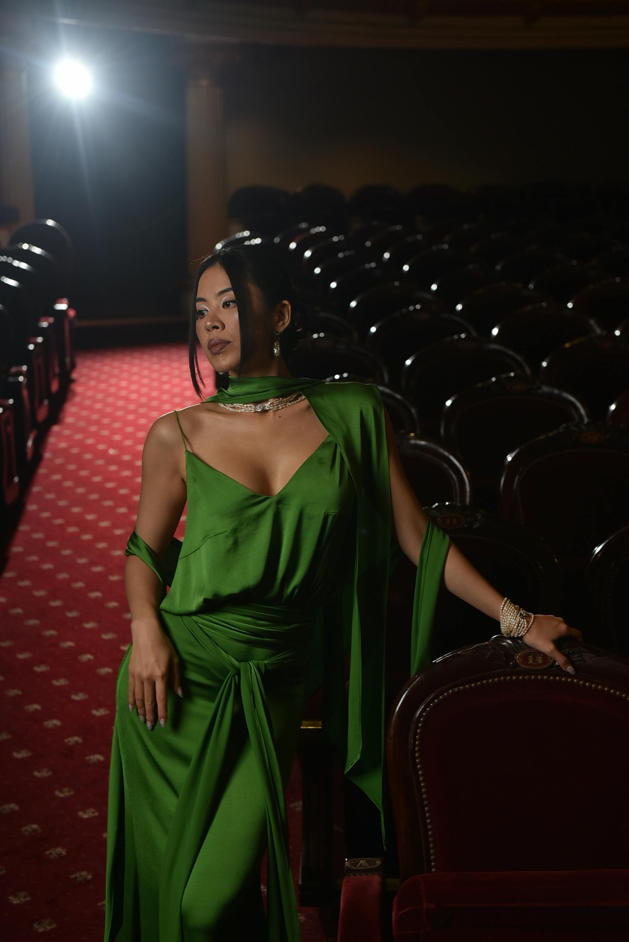 common:alt.prefix Yeşil elbiseli şık kadın, dramatik ışıklandırmanın olduğu boş bir tiyatroda poz veriyor. common:alt.postfix