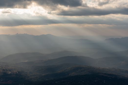 Captivating view of sun rays piercing through clouds over the rolling hills in Minas Gerais, Brazil.