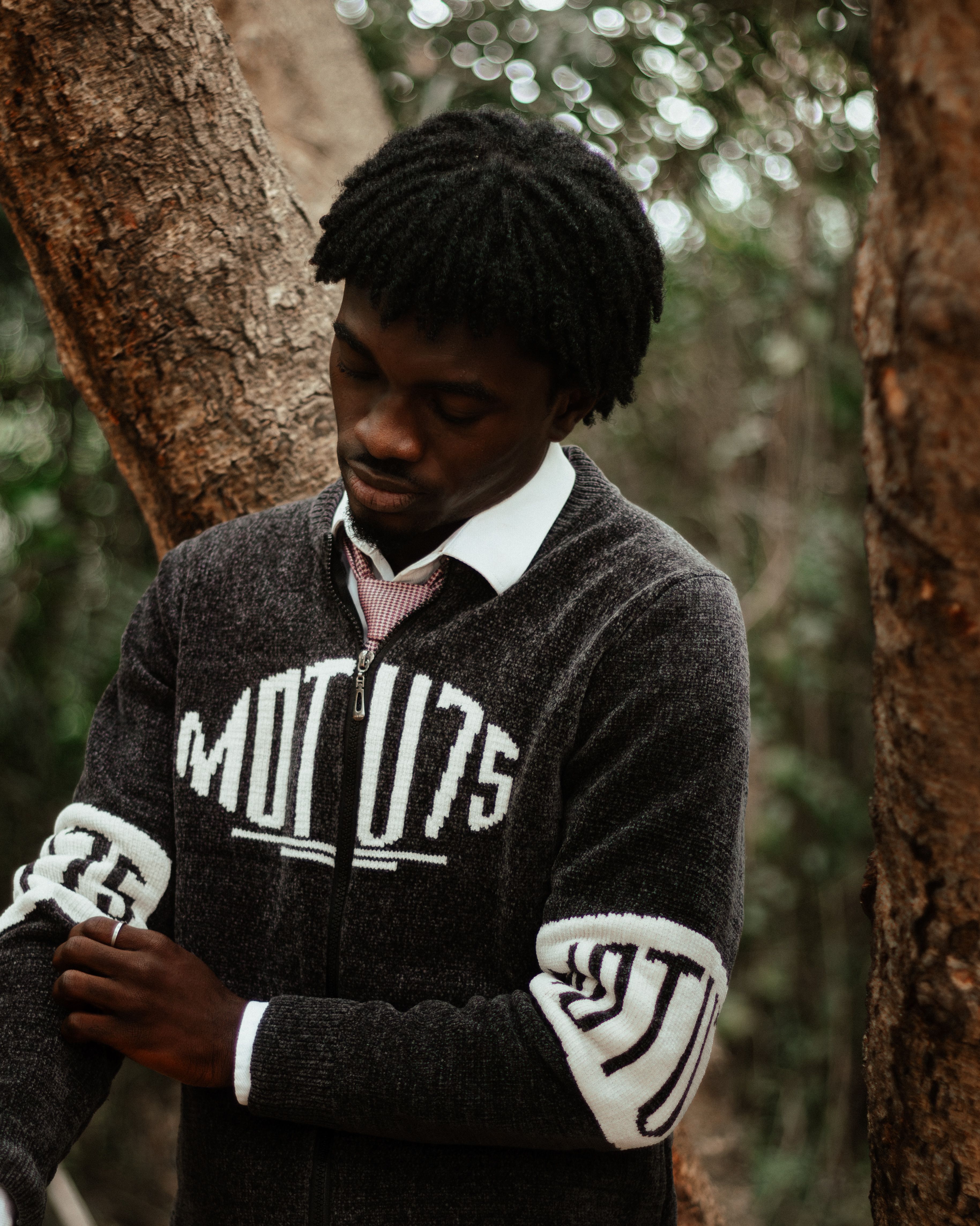 A man in a sweater thoughtfully stands in a wooded area, reflecting a serene moment in nature.
