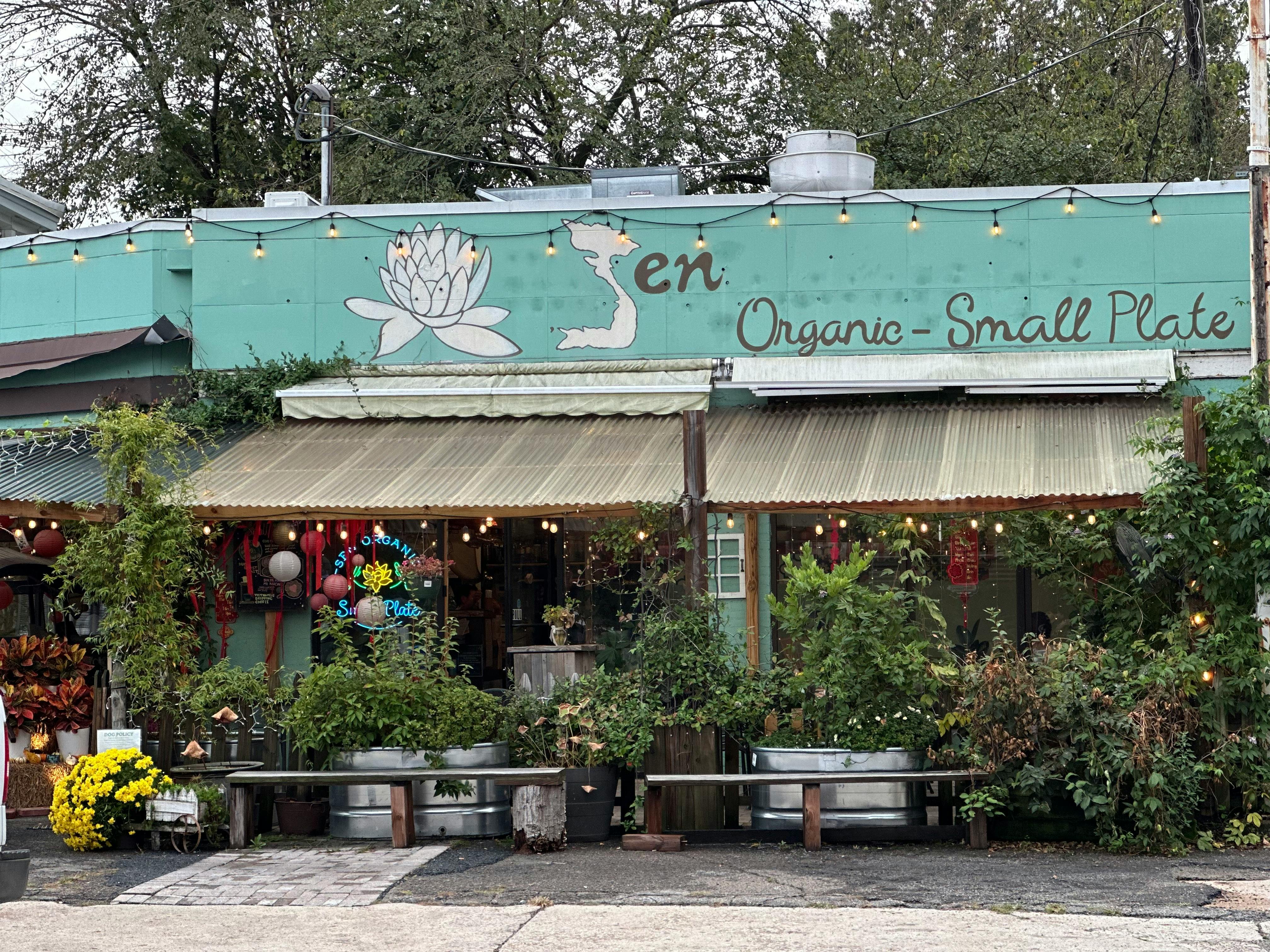 Cozy organic restaurant with green facade and lush plants, perfect for outdoor dining.