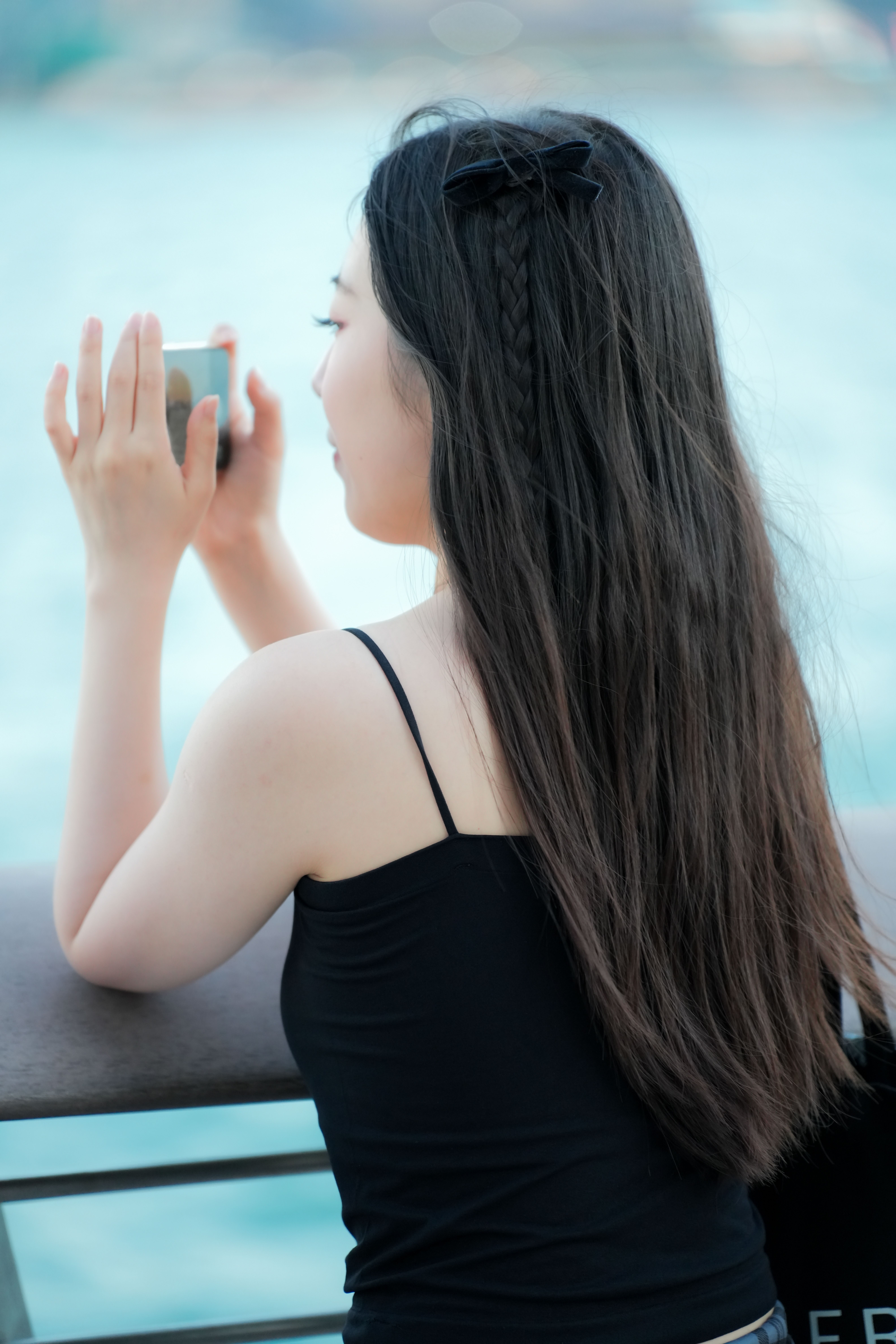A woman takes a photo with her smartphone while overlooking a beautiful waterfront scene.