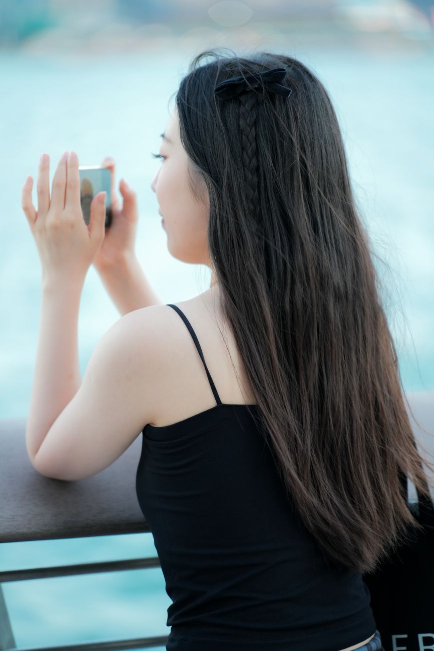A woman takes a photo with her smartphone while overlooking a beautiful waterfront scene.