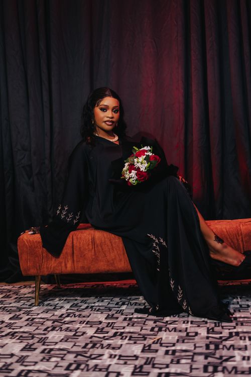 Free Sophisticated woman in a black gown with a floral bouquet seated on an orange sofa indoors. Stock Photo