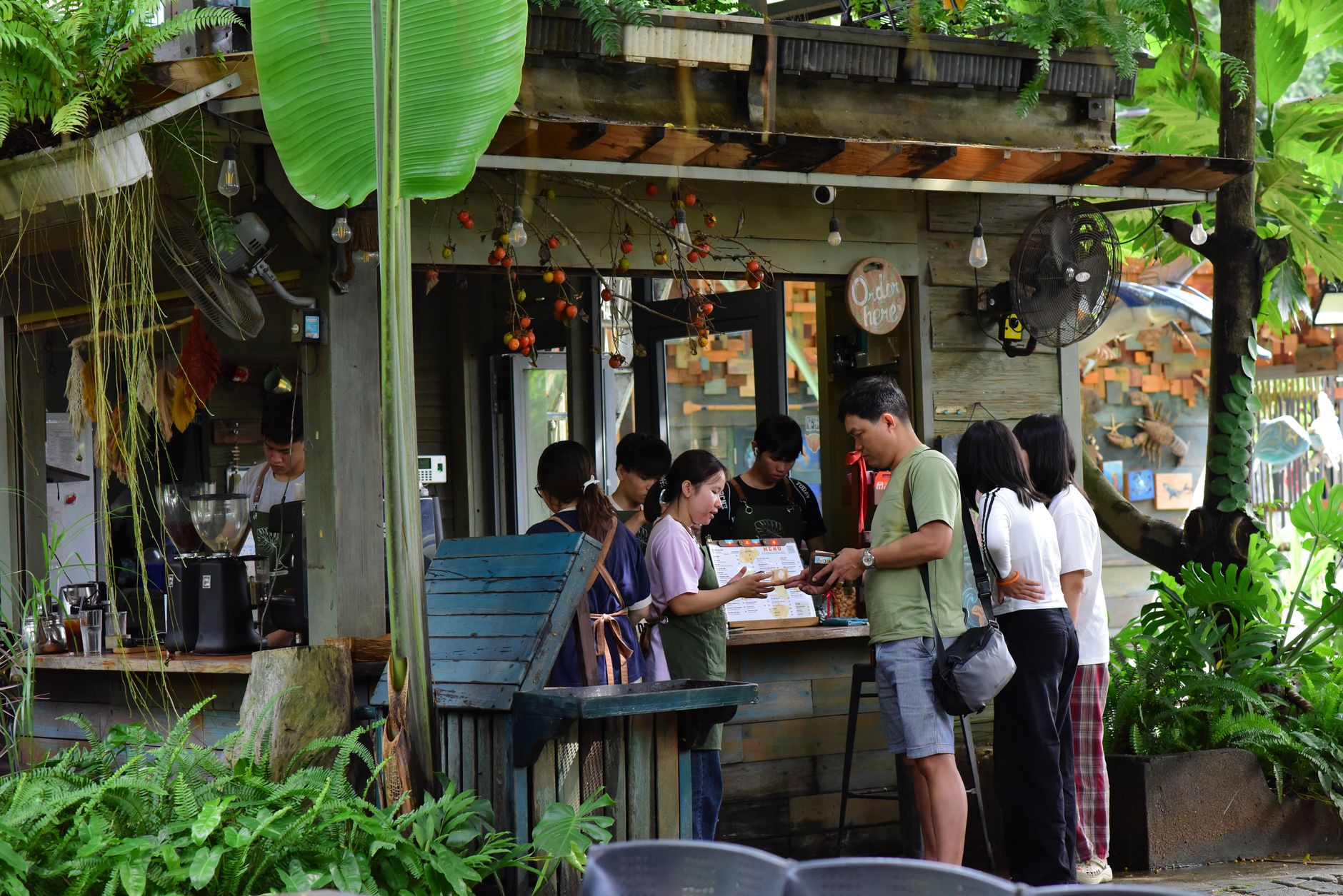 A small group of people gathered at an outdoor coffee shop in a verdant, tropical setting.
