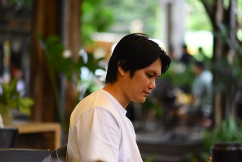 Free A man in a white shirt sitting peacefully outdoors, surrounded by greenery. Stock Photo