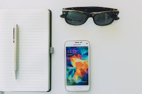 Free White Samsung Smartphone Beside Sunglasses,pen and White Notebook Stock Photo
