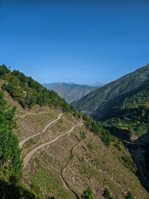 Free A winding mountain road in a lush green valley with towering peaks under a clear blue sky, perfect for nature lovers. Stock Photo