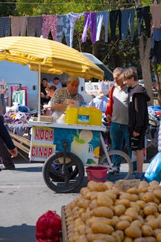 Lively scene of a street vendor selling refreshments at a bustling outdoor market with shoppers browsing.