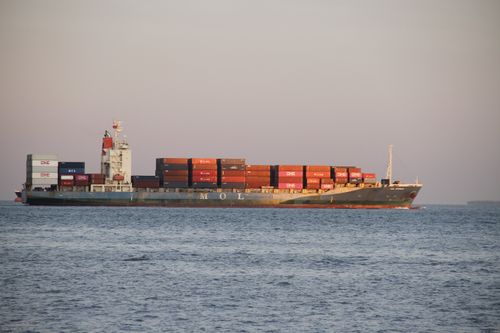 Free A large container ship carrying numerous shipping containers sails across calm waters at sunset. Stock Photo