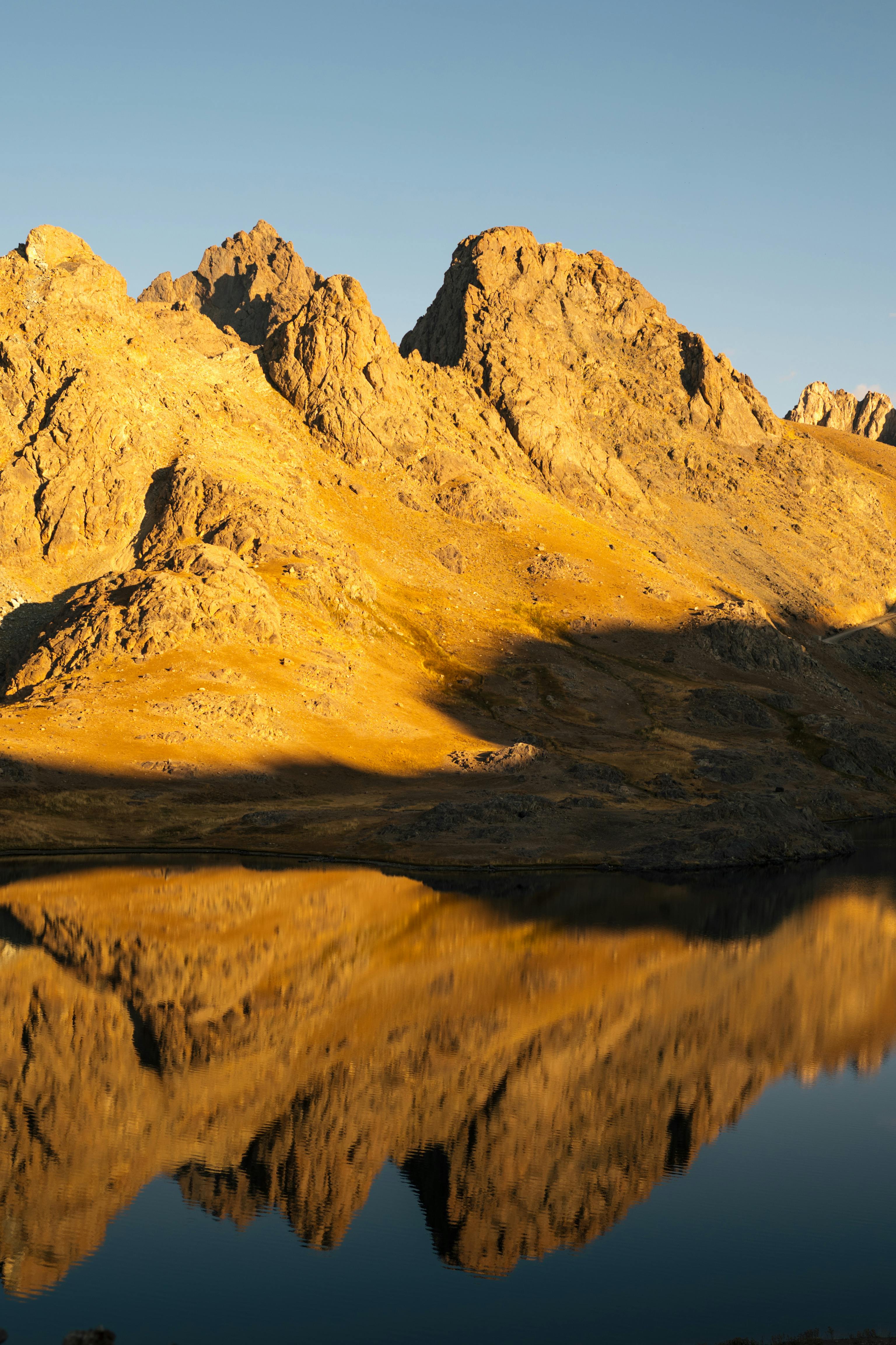 Golden mountains reflecting in a calm lake at sunset, creating a serene and majestic view.
