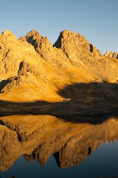 Golden mountains reflecting in a calm lake at sunset, creating a serene and majestic view.