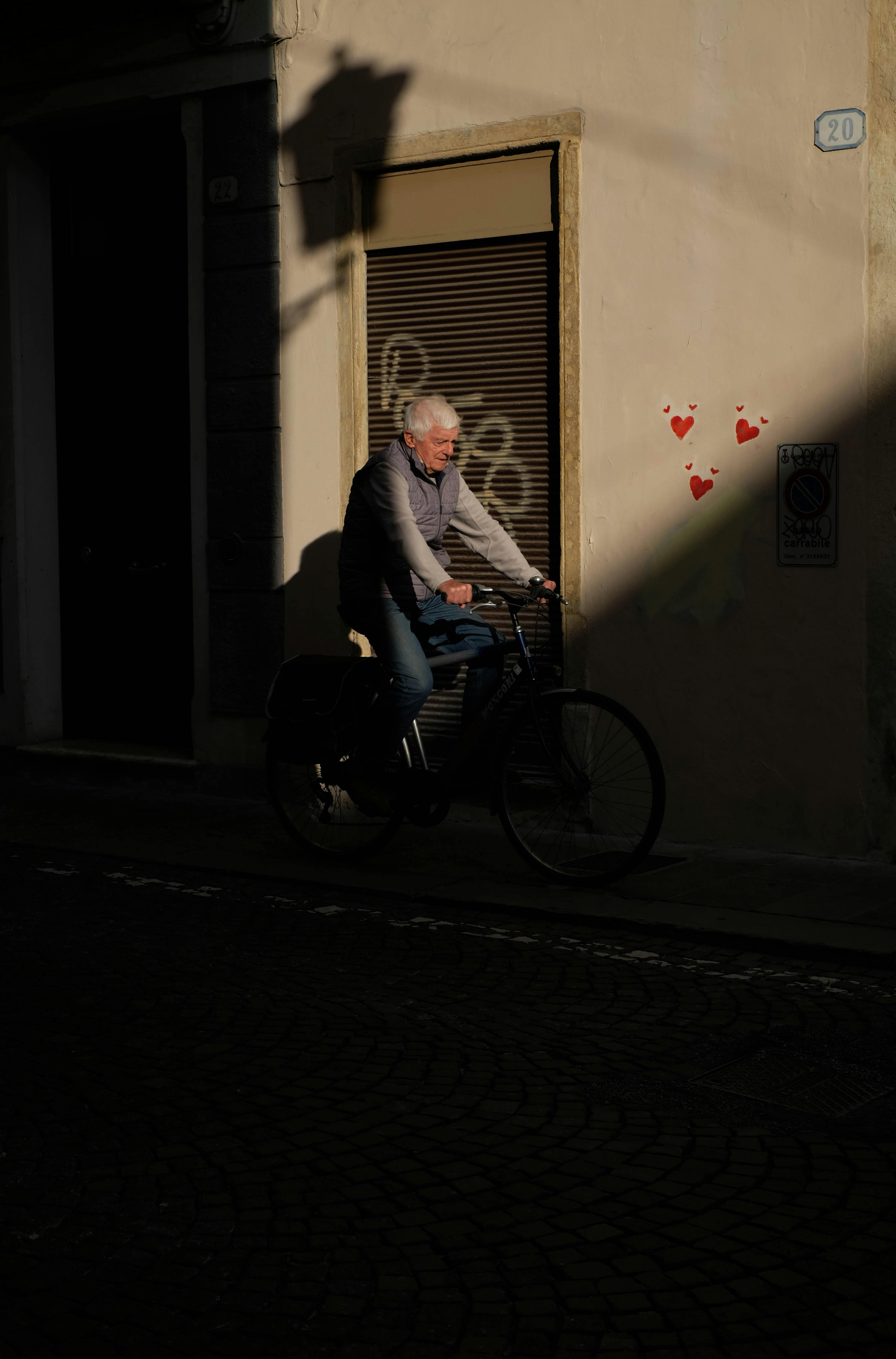 Senior man riding a bicycle in a moody urban setting with heart graffiti on wall