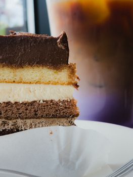 Delicious chocolate layer cake next to an iced coffee in a cafe setting.