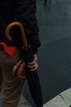 A person holding an umbrella and a bagel on a rainy urban street corner.