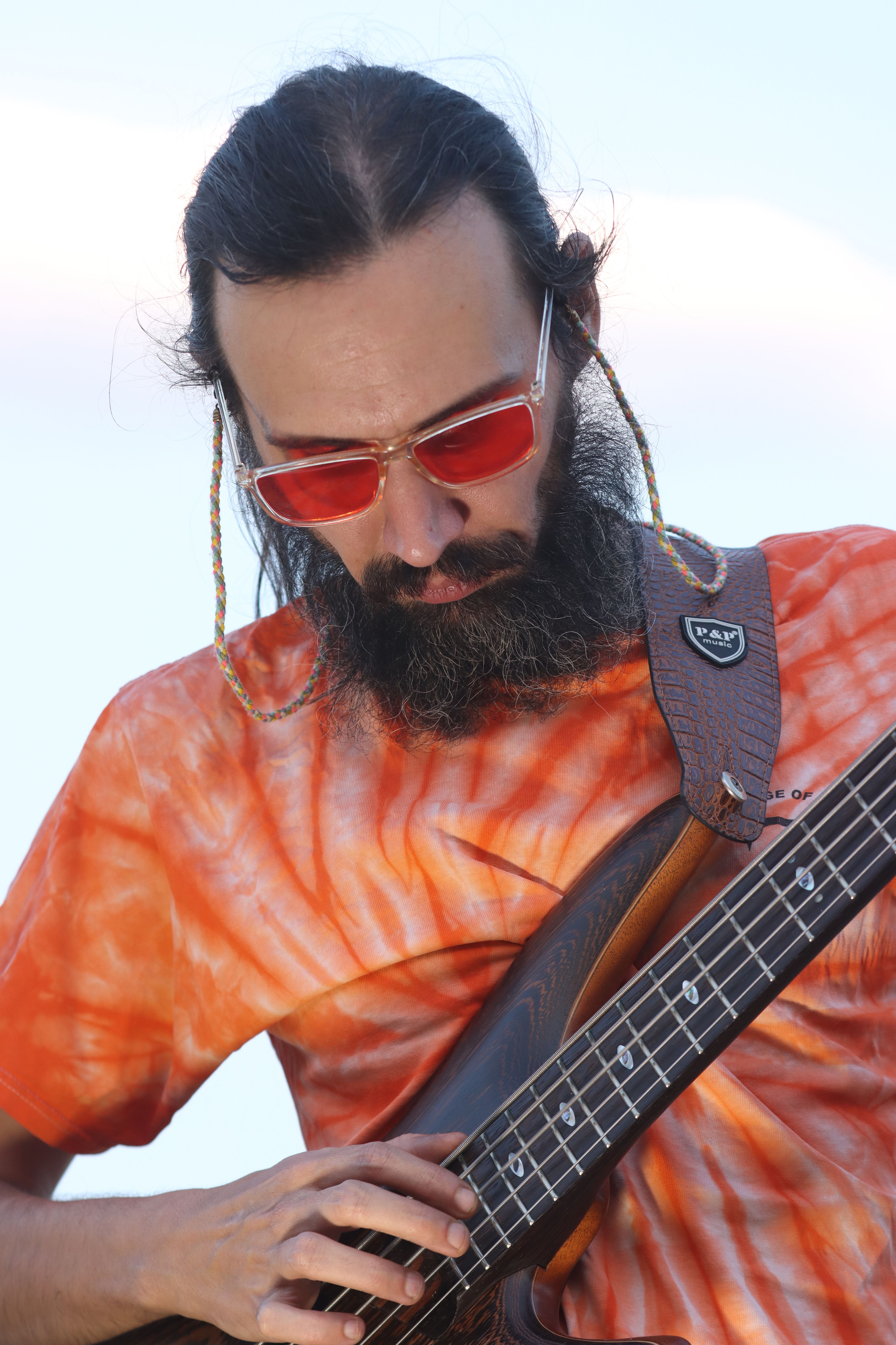A musician with sunglasses playing bass guitar, showcasing modern Iranian music outdoors.