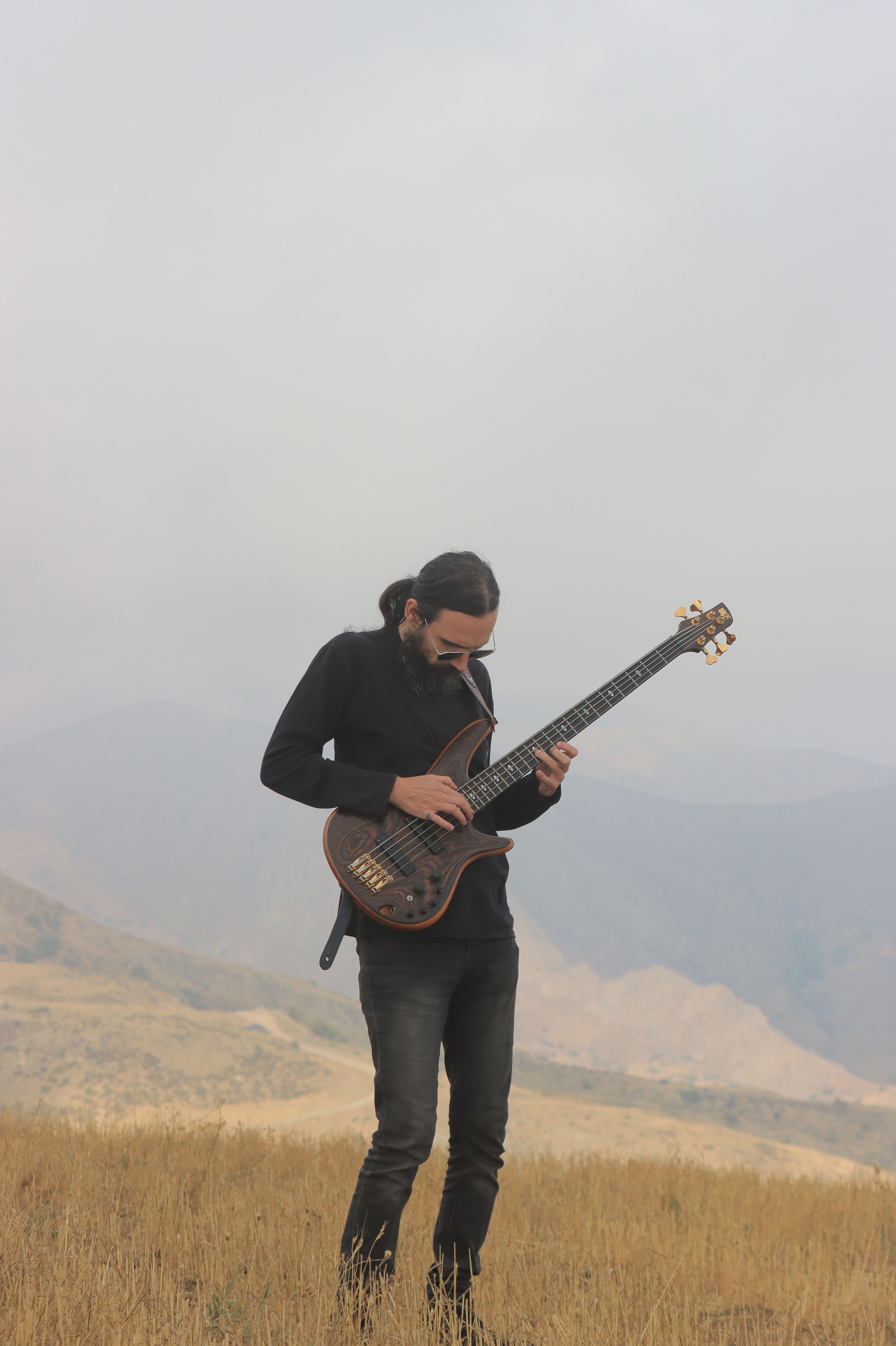 Musician with bass guitar playing outdoors in the scenic hills of Qazvin Province, Iran.