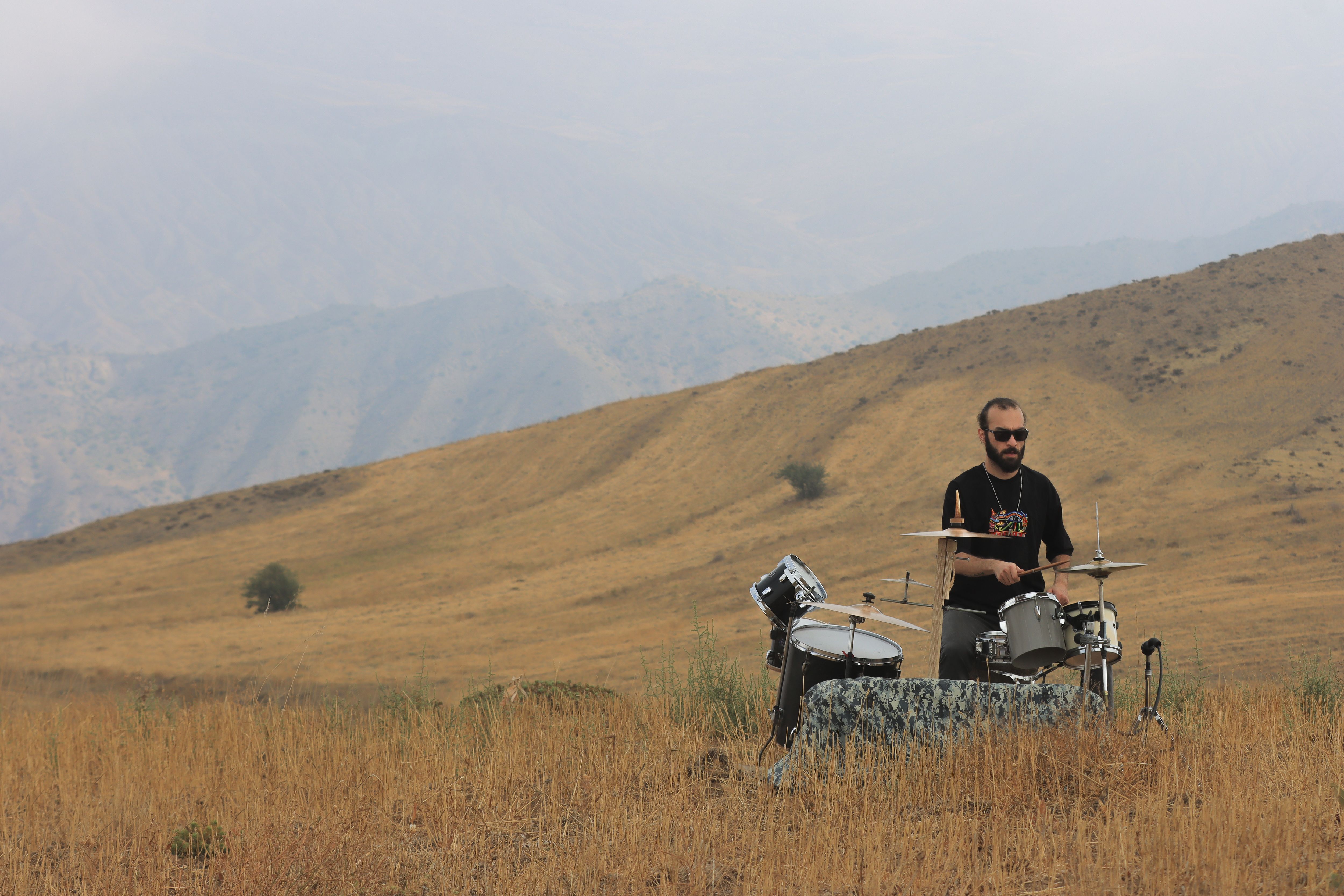 A musician plays drums in the scenic hills of Qazvin, Iran, creating a unique outdoor concert experience.