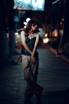 A young woman poses stylishly on a city street at night, illuminated by urban lights.