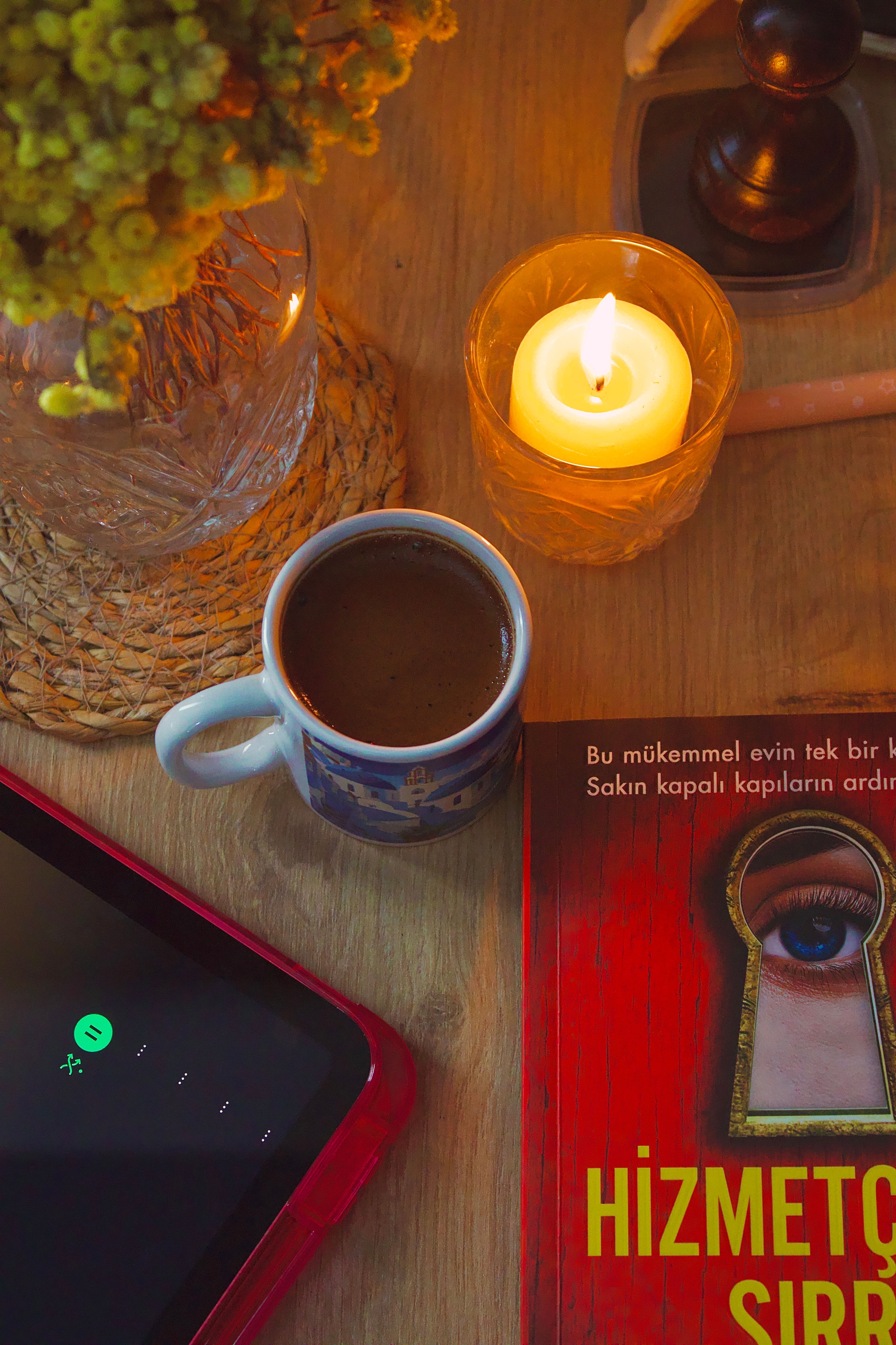 Warm cozy setup with coffee, candle, and book on a wooden table.