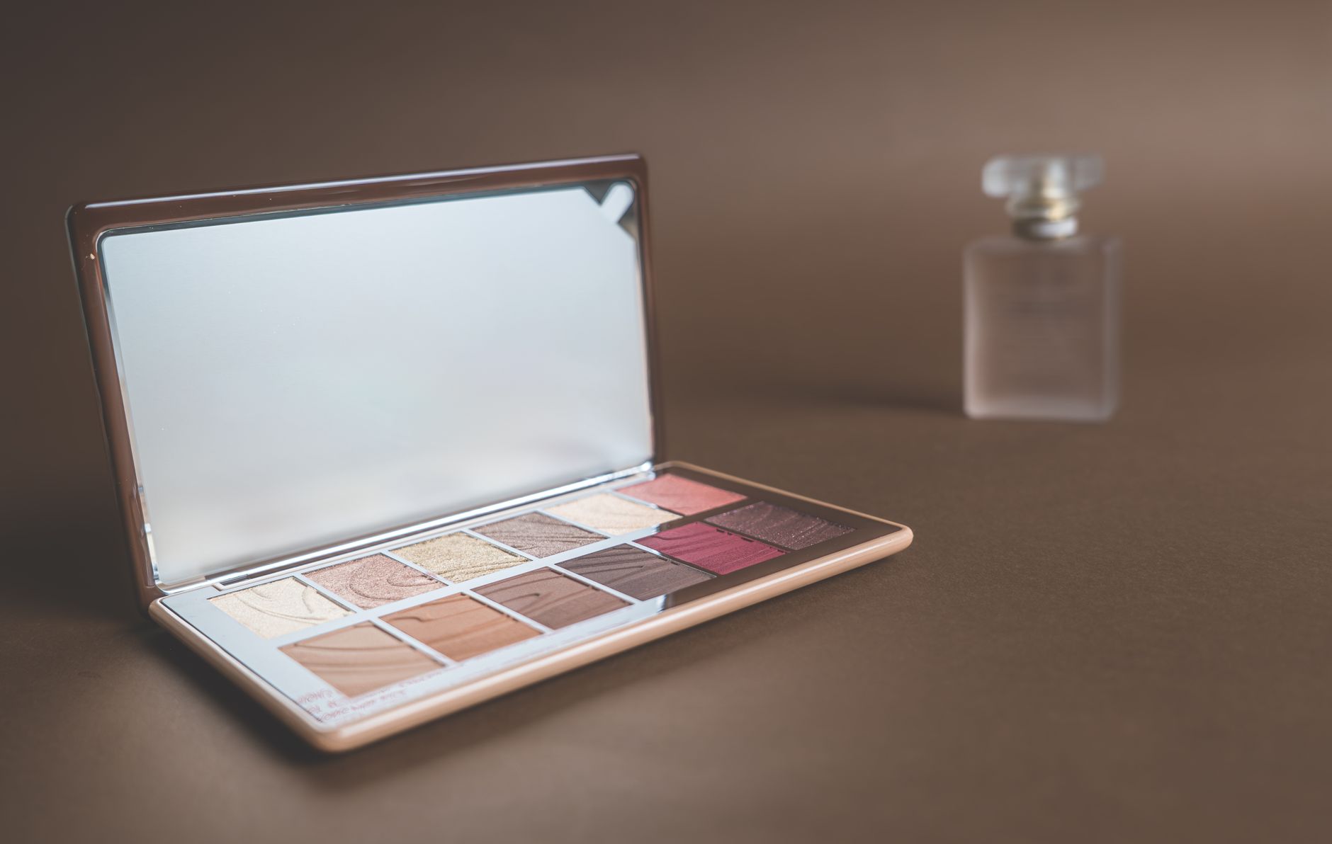 Stylish makeup palette and perfume bottle on a brown background. Ideal for beauty and fashion imagery.