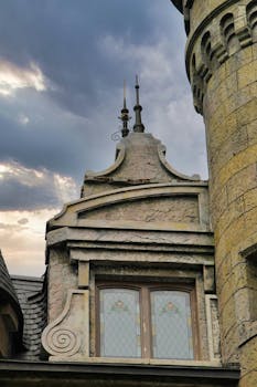 Close-up of a vintage castle turret with intricate details against a moody sky.
