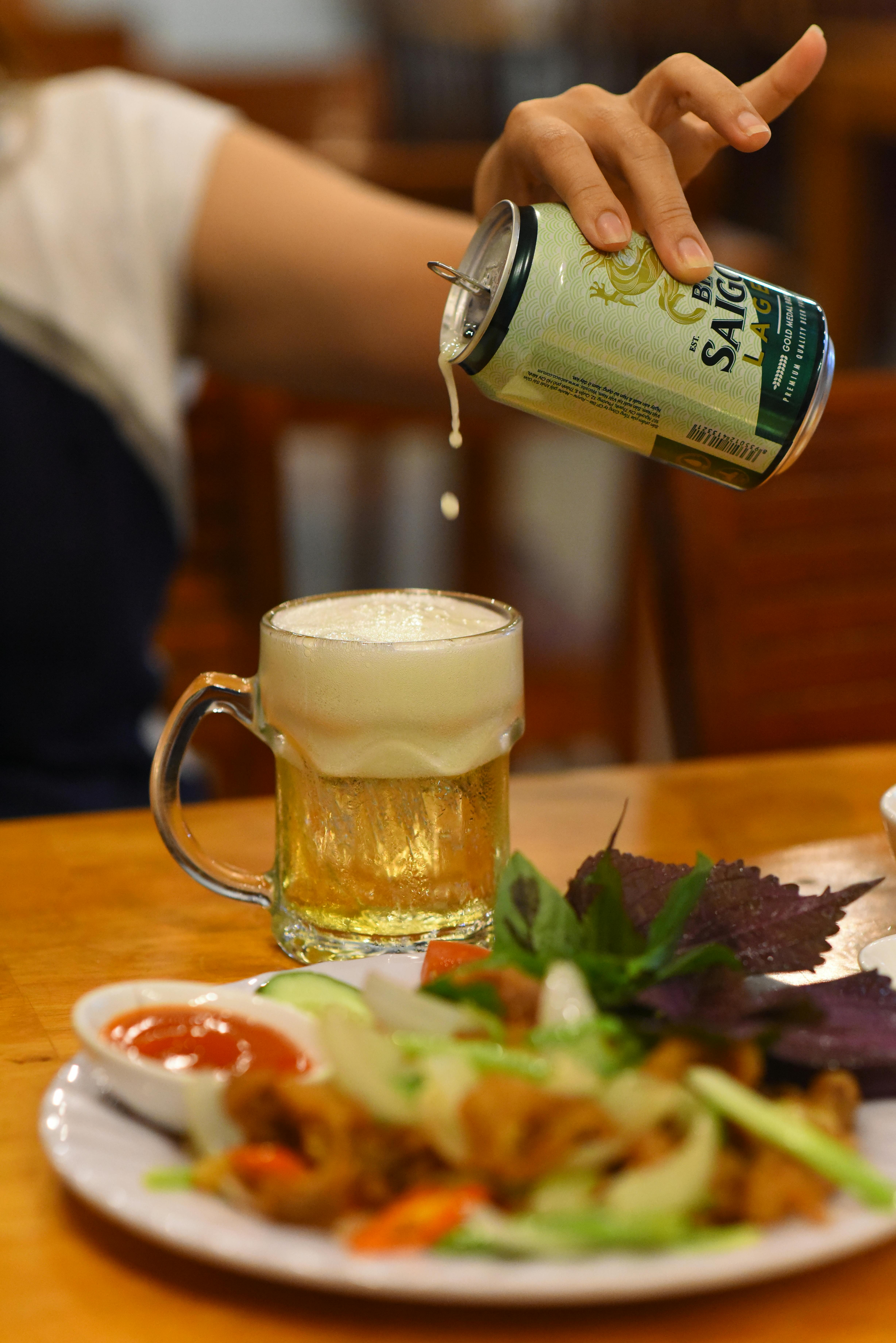 A refreshing mug of beer being poured, paired with a colorful Asian meal featuring vegetables and herbs.