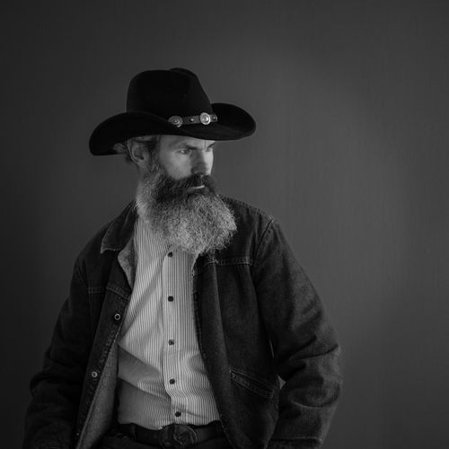 Free Black and white portrait of a bearded cowboy wearing a hat and jacket, exuding a classic Western feel. Stock Photo