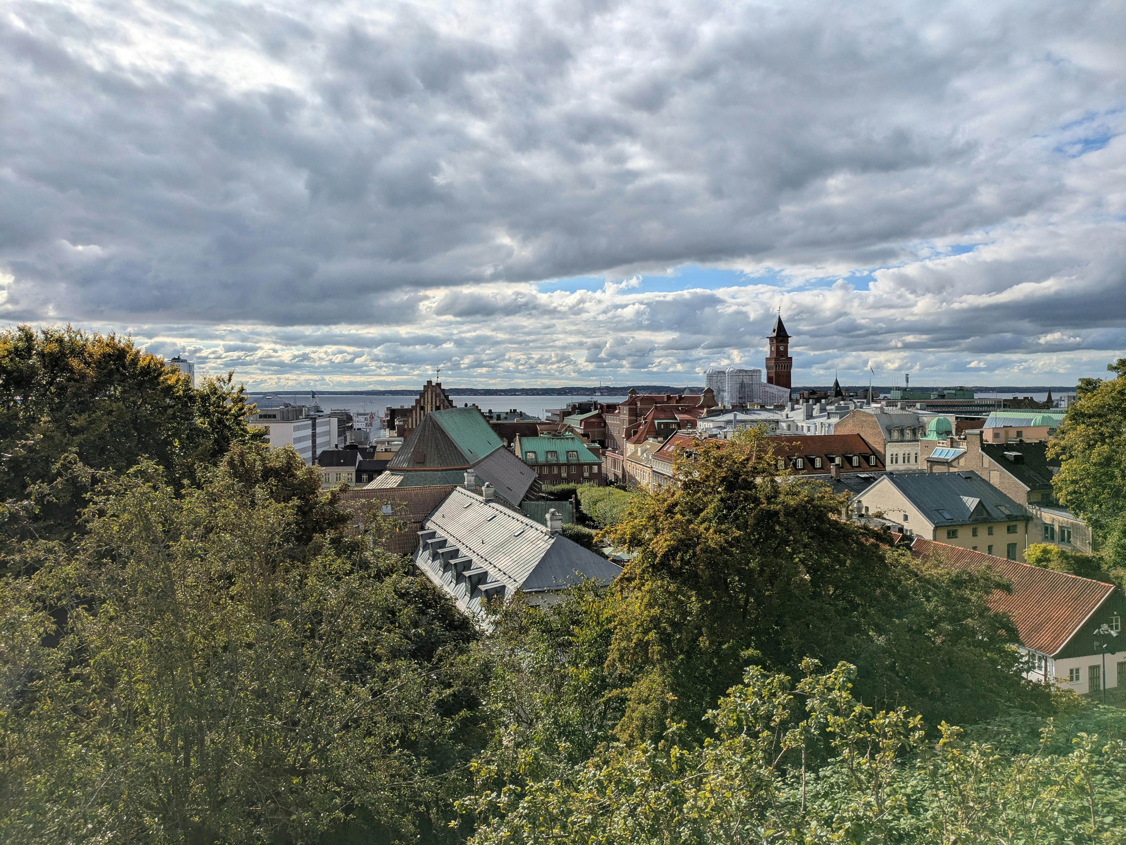 A panoramic view of a European cityscape featuring historic buildings and lush greenery under a cloudy sky.