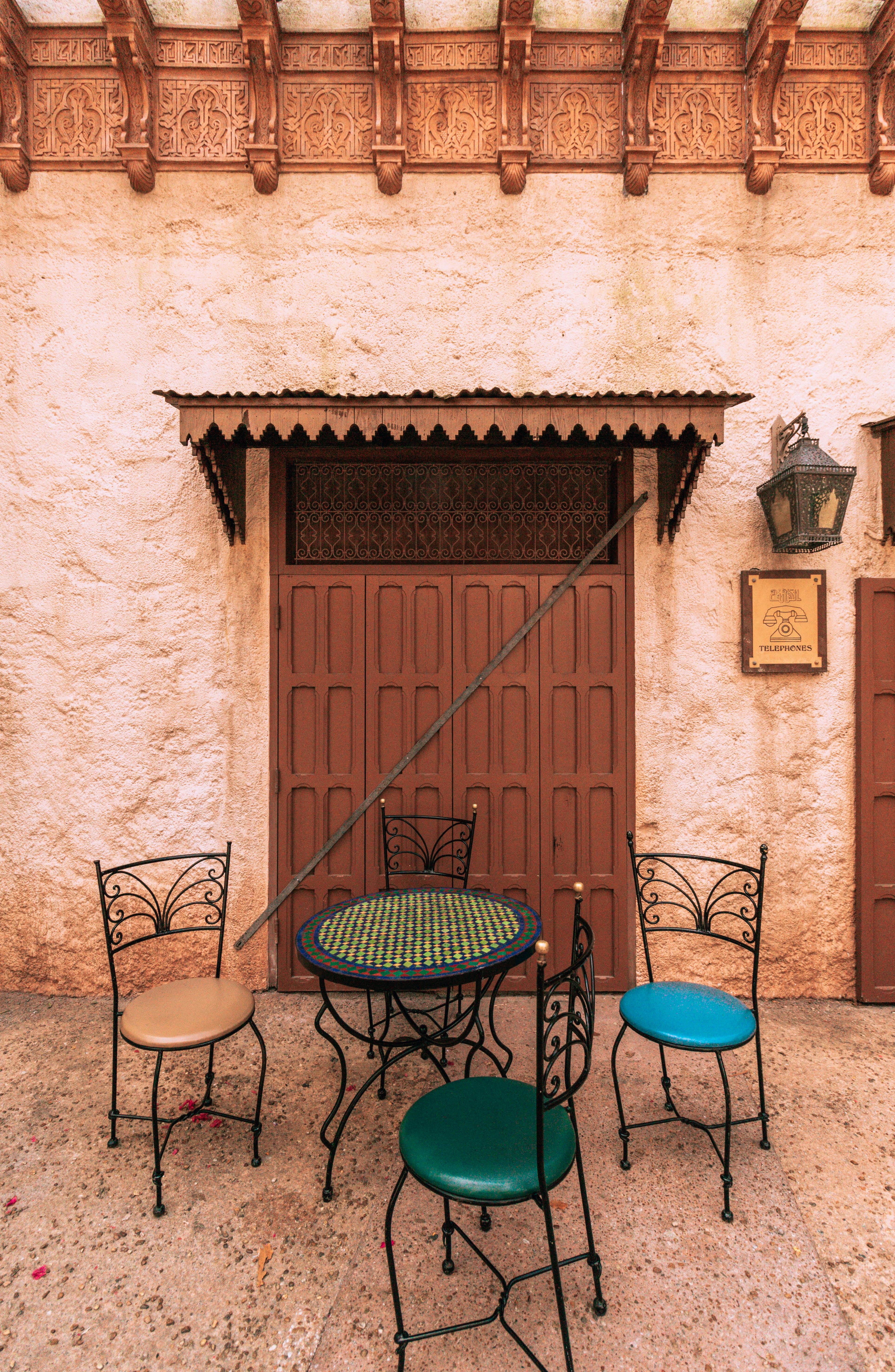 Inviting Moroccan-style patio with ornate metal chairs and a textured wall in a theme park setting.