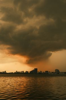 A dramatic cityscape of Tokyo with dark storm clouds at sunset, reflecting over the water.
