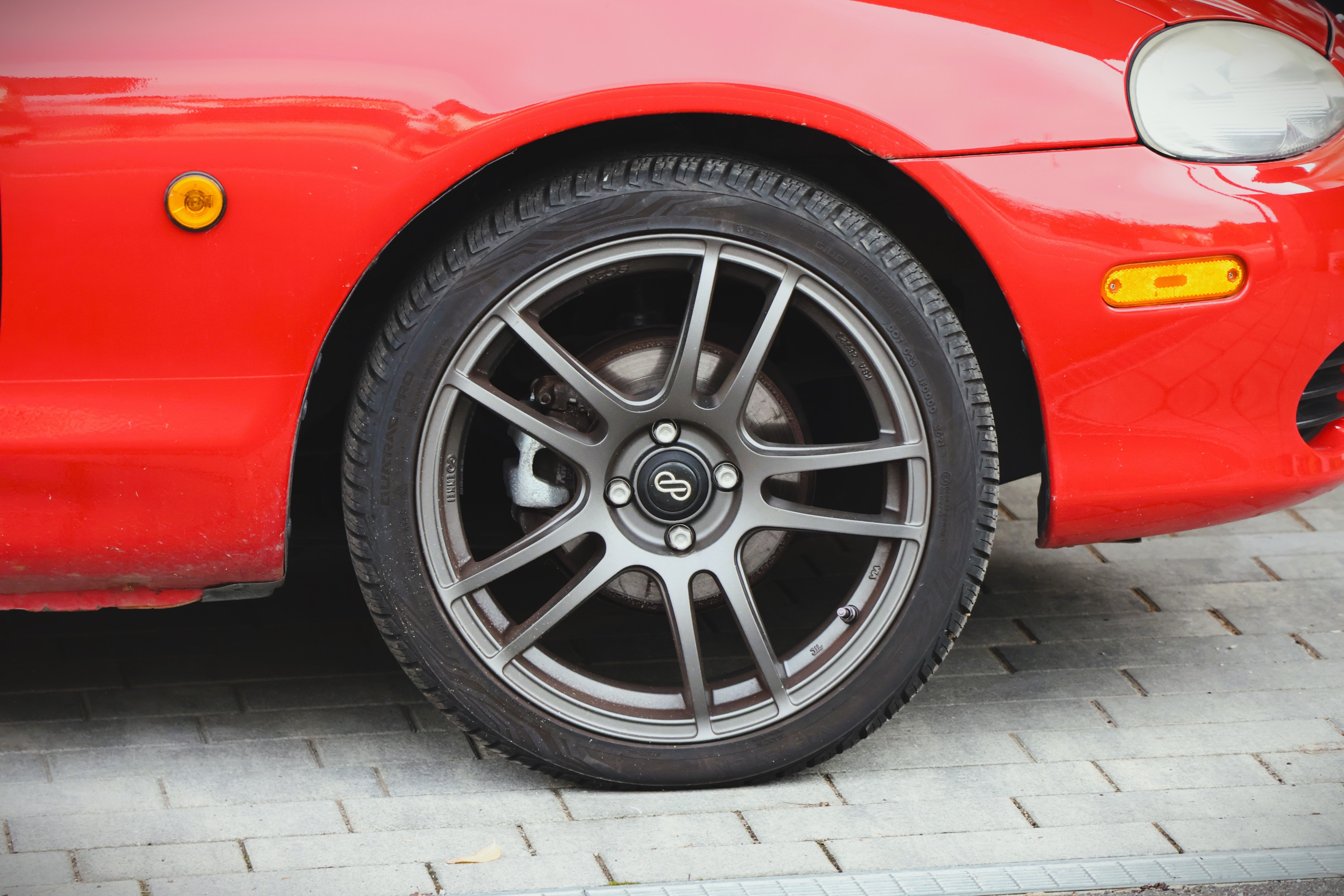 Detailed shot of a red car with alloy wheel parked on a pavement, showcasing automotive design.