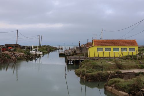 Free A serene view of a coastal fishing village featuring a vibrant yellow house by a quiet channel. Stock Photo