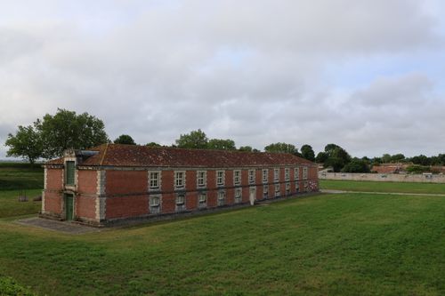 Free A long historic brick building in a green landscape under a cloudy sky. Stock Photo