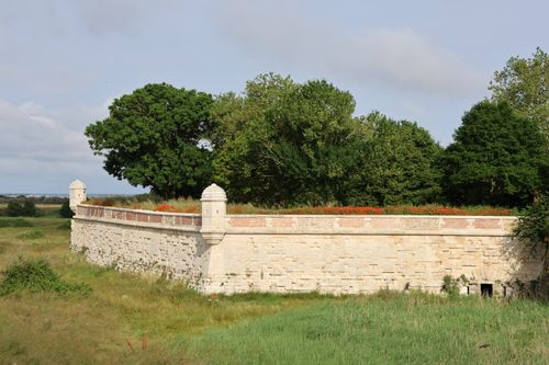 Free A historic stone wall surrounded by lush trees and grass under a blue sky. Stock Photo