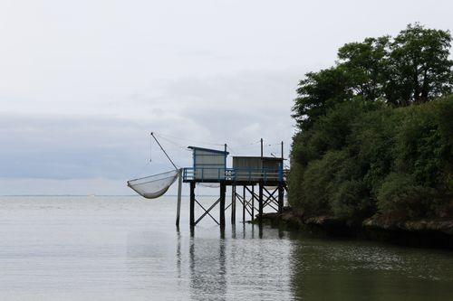 Free A serene coastal scene with a fishing hut on stilts by the water and lush greenery. Stock Photo